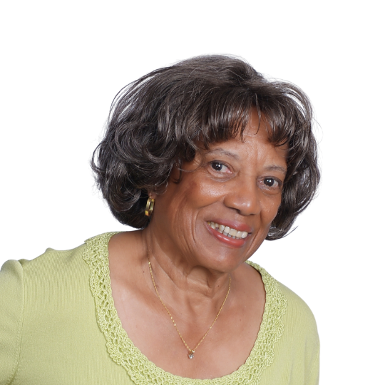 Brenda Goburn Smith smiles at the camera. She has short, wavy gray hair and wears a light green sweater with a scalloped neckline, small hoop earrings, and a delicate gold necklace. The background is plain white. Brenda Goburn Smith, Certified Coach & Resume Writer